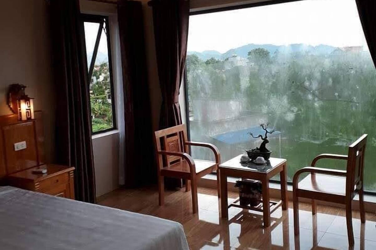 A hotel room with a bed, a desk, a chair, a small table with a decorative item, and a view of the outdoors through a large window.