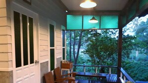 A covered outdoor seating area with wooden chairs and a table, overlooking a lush garden.