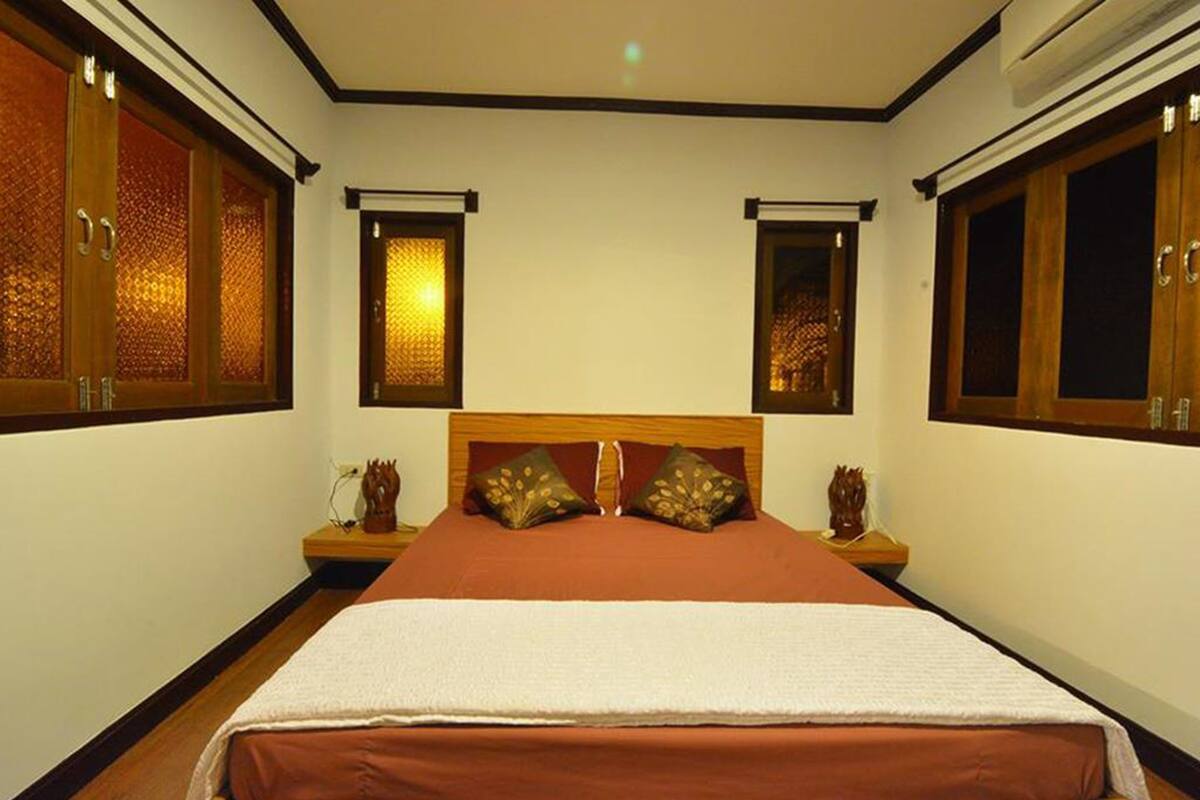 A bedroom with a large bed, two nightstands, a wooden headboard, and two windows with decorative glass panels.