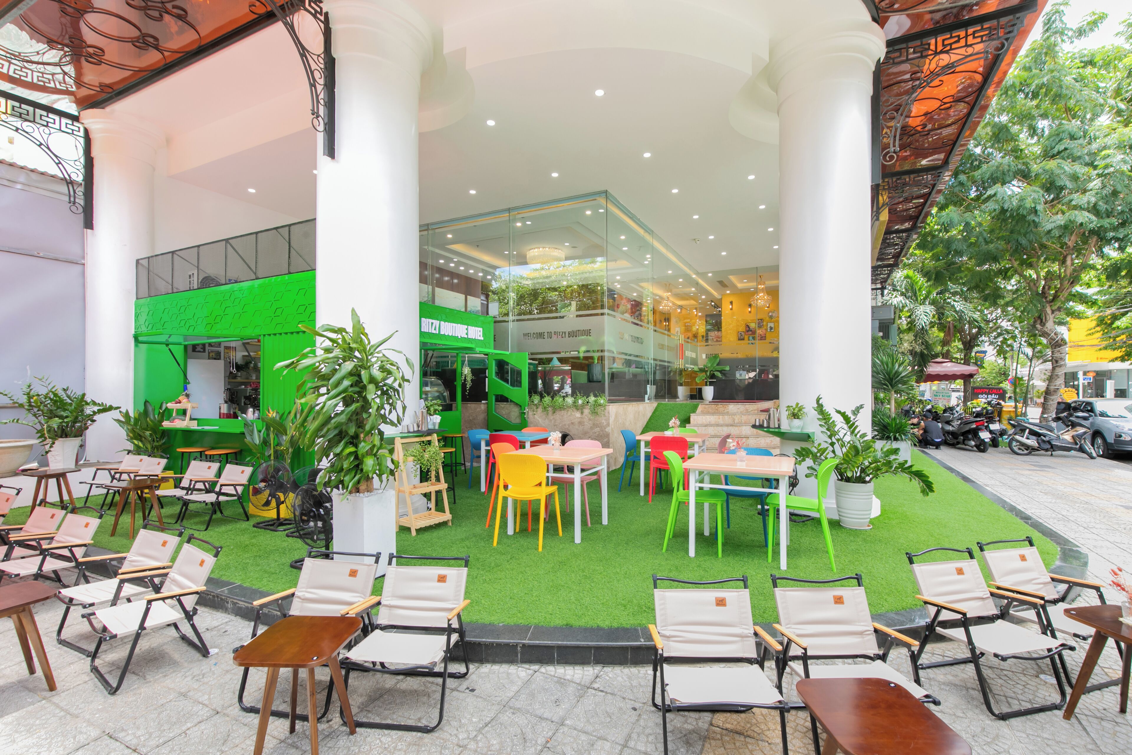 A rooftop café with outdoor seating, a green area, and a view of a shopping mall.