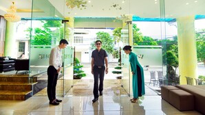 A modern hotel lobby with glass doors, a reception desk, and a seating area with a sofa and chairs. - Ritzy Boutique Hotel Da Nang (Da Nang)