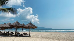 A beach with thatched umbrellas and wooden lounge chairs. - Ritzy Boutique Hotel Da Nang (Da Nang)