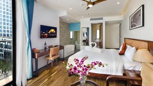 A hotel room with a bed, a desk, a chair, a TV, a ceiling fan, and a window with curtains. - Ritzy Boutique Hotel Da Nang (Da Nang)