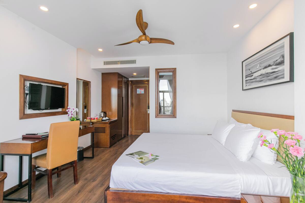 A hotel room with a bed, desk, chair, television, and a ceiling fan.