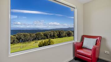A room with a large window offering a view of a coastal landscape, a red leather chair, and a white wall.