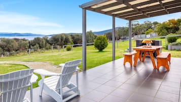 Un patio techado con vista a un lago y colinas, con una mesa y sillas.