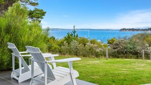 A patio with two white Adirondack chairs and a table, overlooking a grassy area and a body of water. - Manfield Seaside Bruny Island (Alonnah)