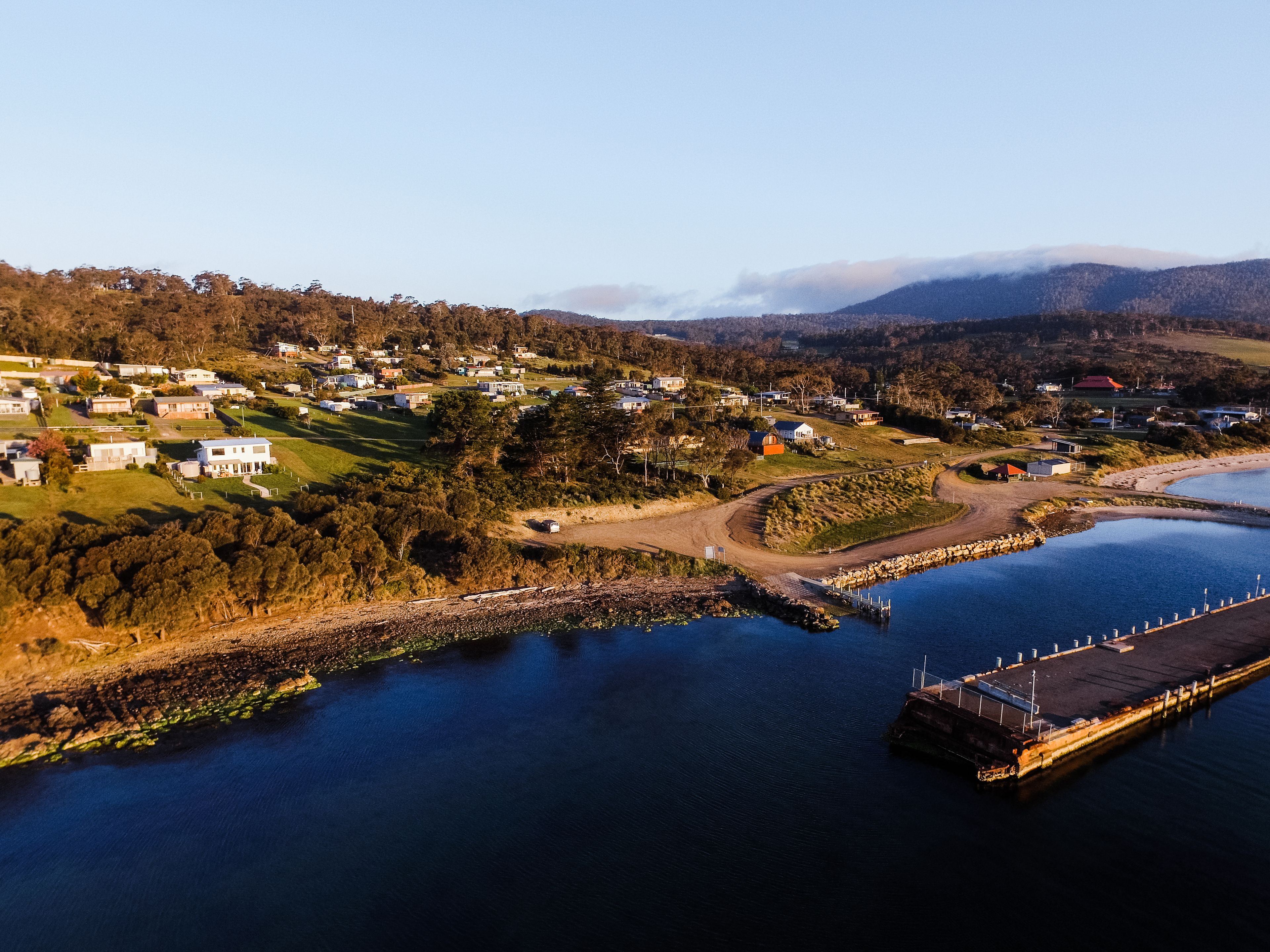An aerial view of a coastal town with houses, a dock, and a clear sky.