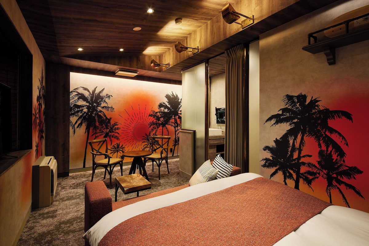 A hotel room with a bed, a desk, a chair, and a wall mural.