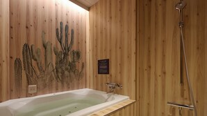 Une salle de bain aux murs lambrissés, dotée d’une baignoire, d’une douche et d’une décoration murale représentant des cactus.