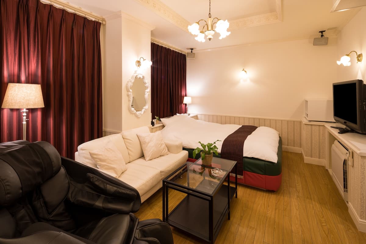 A hotel room with a bed, a sofa, a coffee table, a TV, and a lamp.
