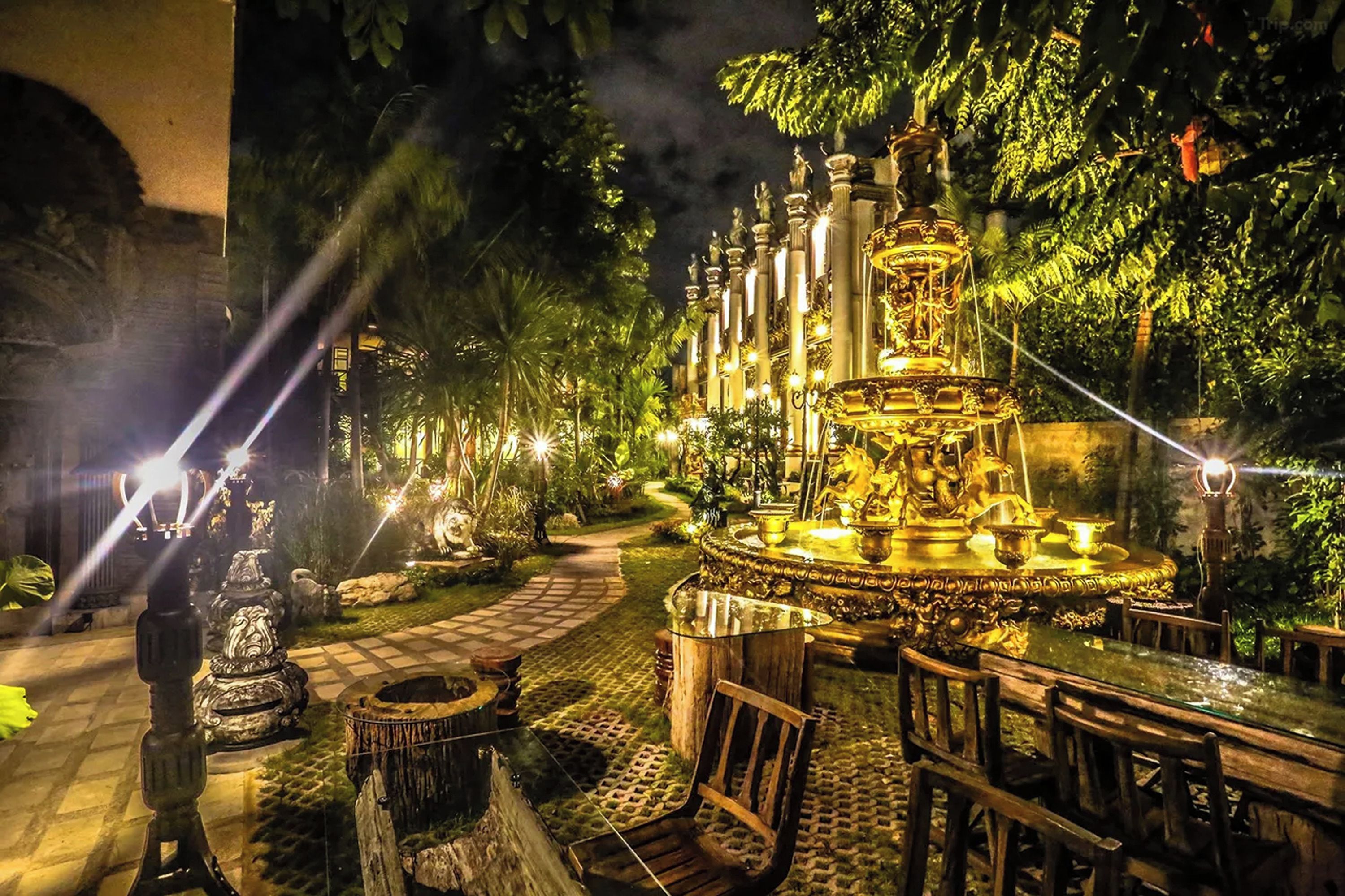 A nighttime garden with a central fountain, surrounded by stone benches and pathways.