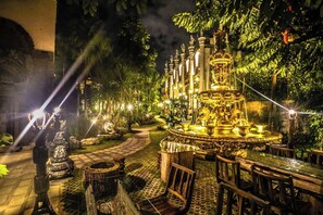 A nighttime garden with a central fountain, surrounded by stone benches and pathways.