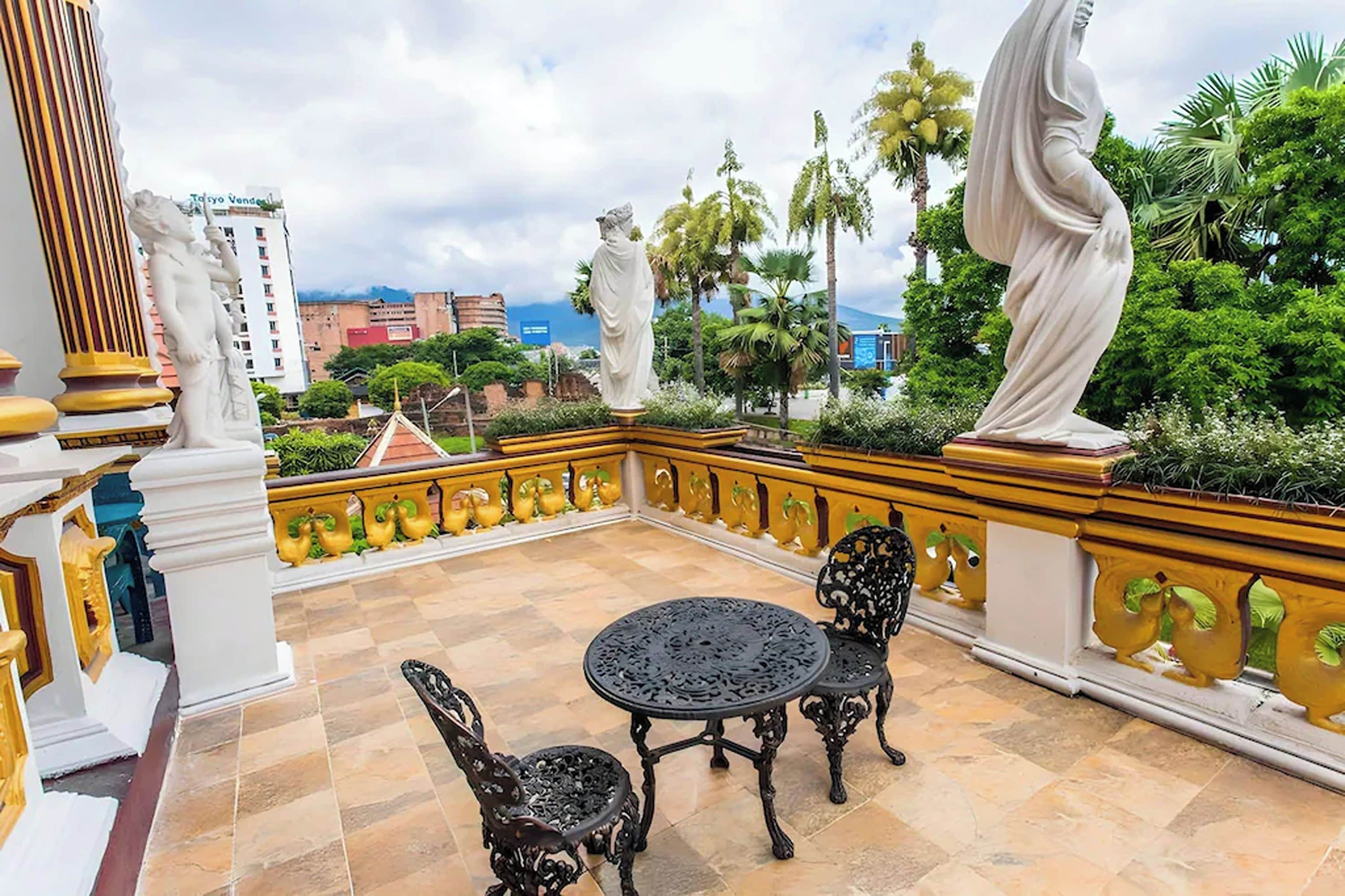 Una terraza con mesa y sillas, una estatua y vistas de la ciudad.