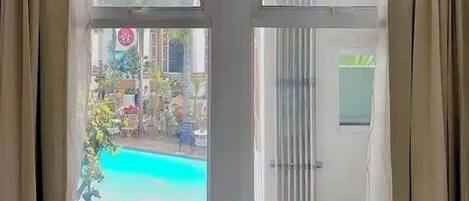 Una stanza con un'ampia porta scorrevole in vetro che dà su una zona esterna con piscina e vegetazione.