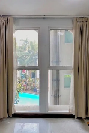Une pièce dotée d’une grande porte-fenêtre coulissante donnant sur un espace extérieur avec une piscine et de la verdure.