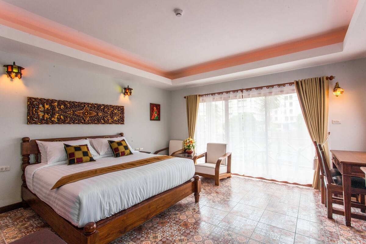 Une chambre d’hôtel avec un grand lit, un bureau et une chaise. Il y a une fenêtre avec des rideaux et une vue sur l’extérieur.