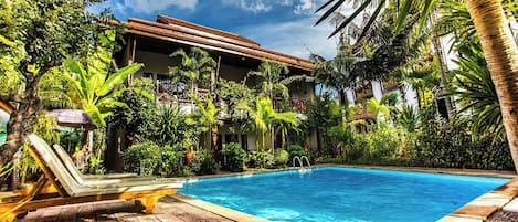 Un espace piscine doté d’une terrasse en bois, de chaises longues et d’une végétation tropicale.