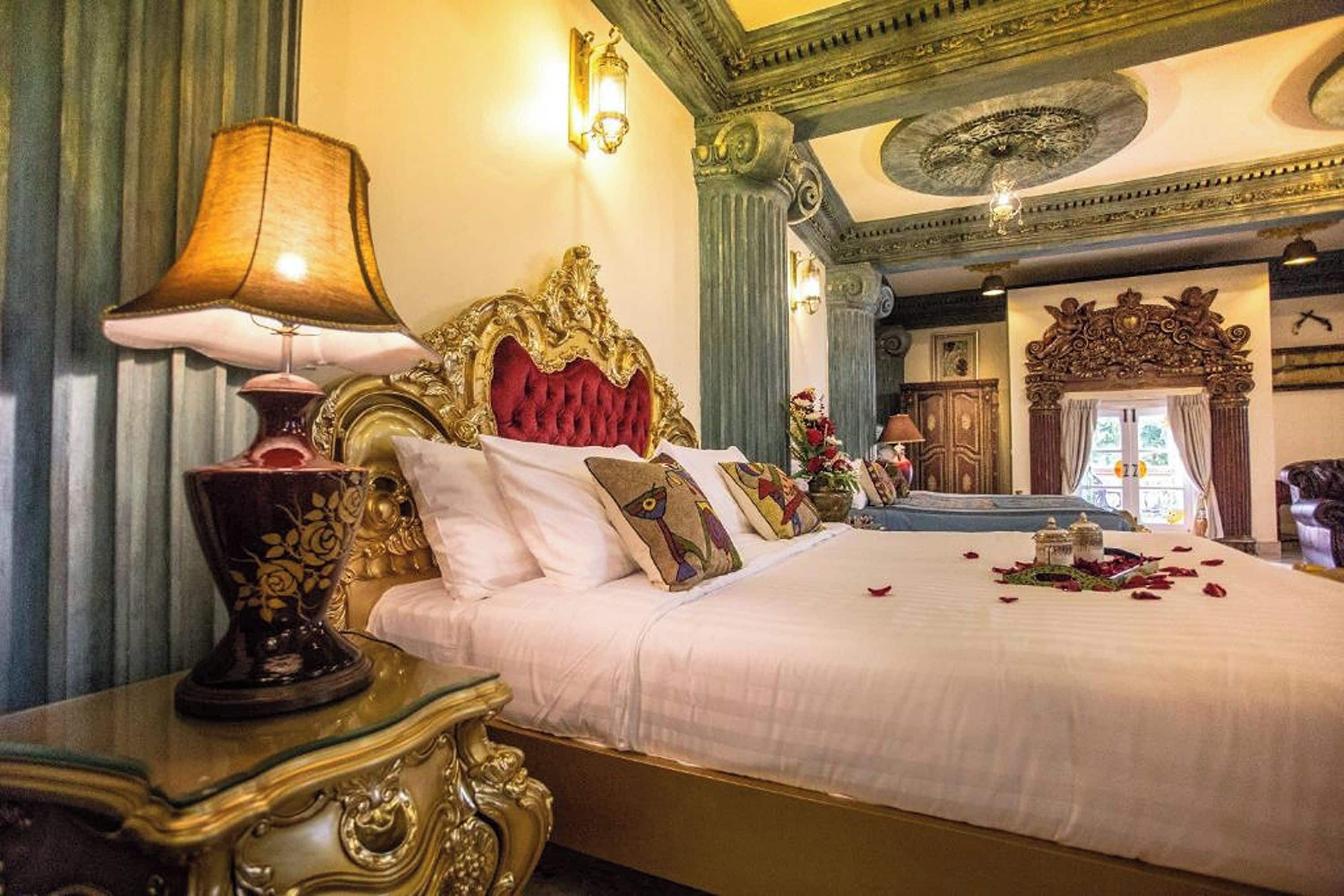 A luxurious bedroom with an ornate bed, a decorative lamp, and elegant wall sconces.