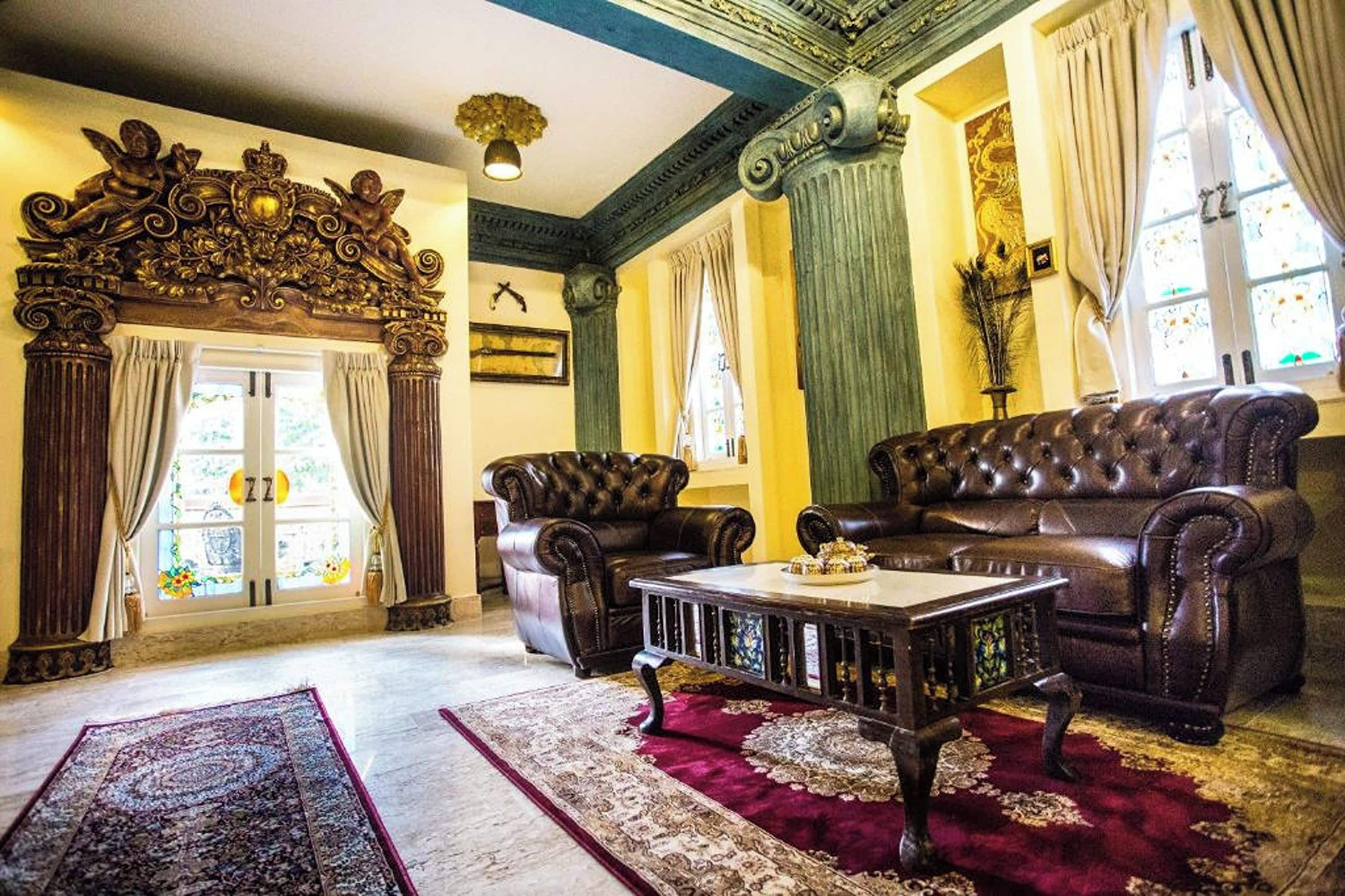 A room with a large ornate fireplace, leather sofas, a coffee table, and a patterned rug.