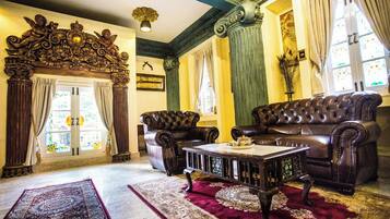 A room with a large ornate fireplace, leather sofas, a coffee table, and a patterned rug.
