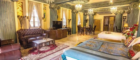 A luxurious hotel room with a large bed, a sofa, a television, and a dining area.