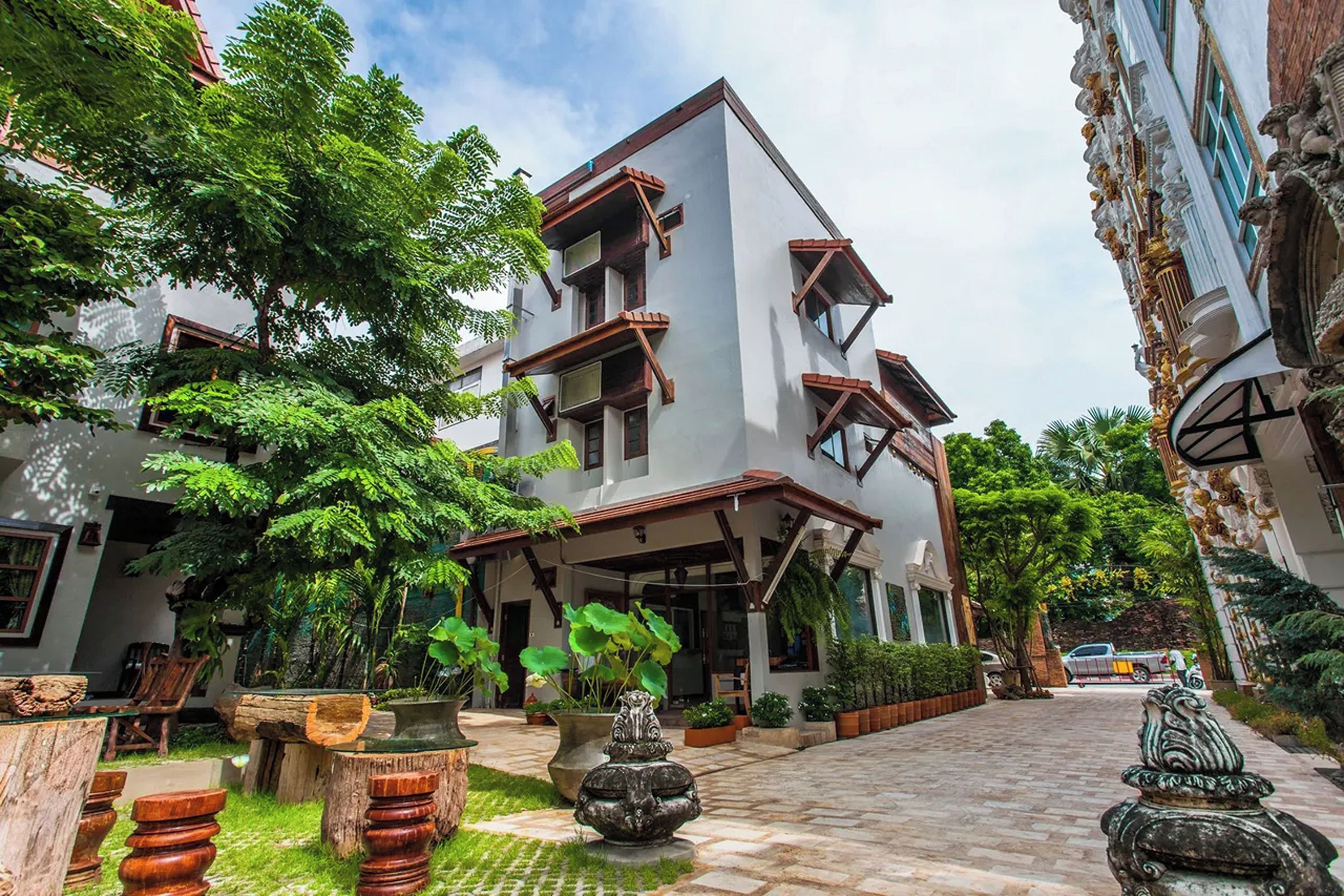 Un bâtiment à deux étages doté d’un balcon, entouré d’une végétation luxuriante et bordé d’un chemin pavé.