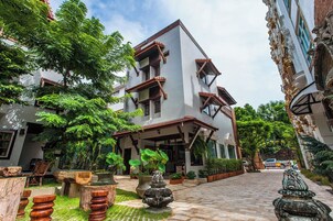 Un edificio de dos pisos con balcón, rodeado de exuberante vegetación y un sendero pavimentado.