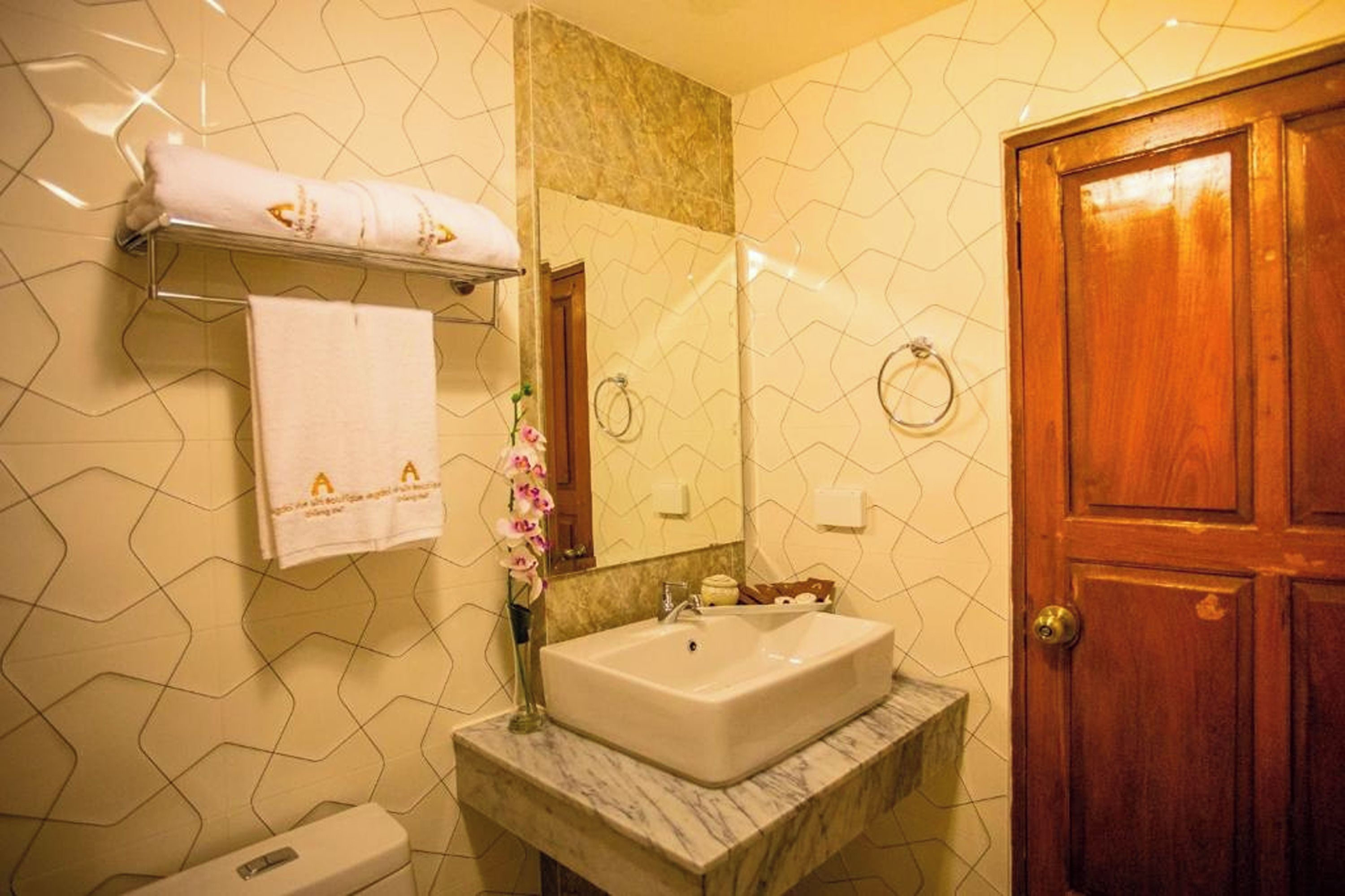 Un baño con lavamanos de mármol, un perchero con una toalla blanca, un espejo y una puerta de madera.