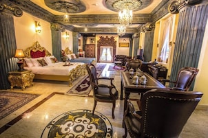 A luxurious hotel room with a large bed, a sitting area with a table and chairs, and a chandelier.