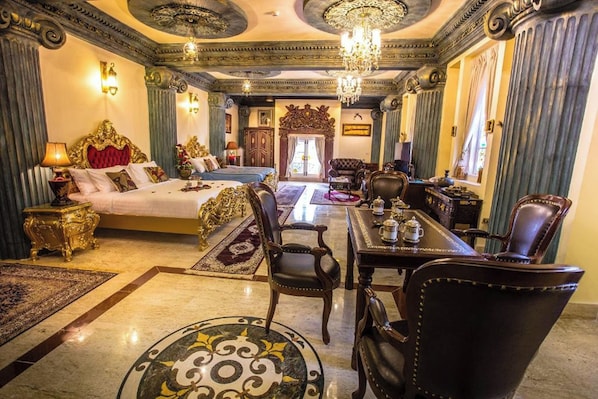 Une chambre d’hôtel luxueuse avec un grand lit, un coin salon avec une table et des chaises, et un lustre.