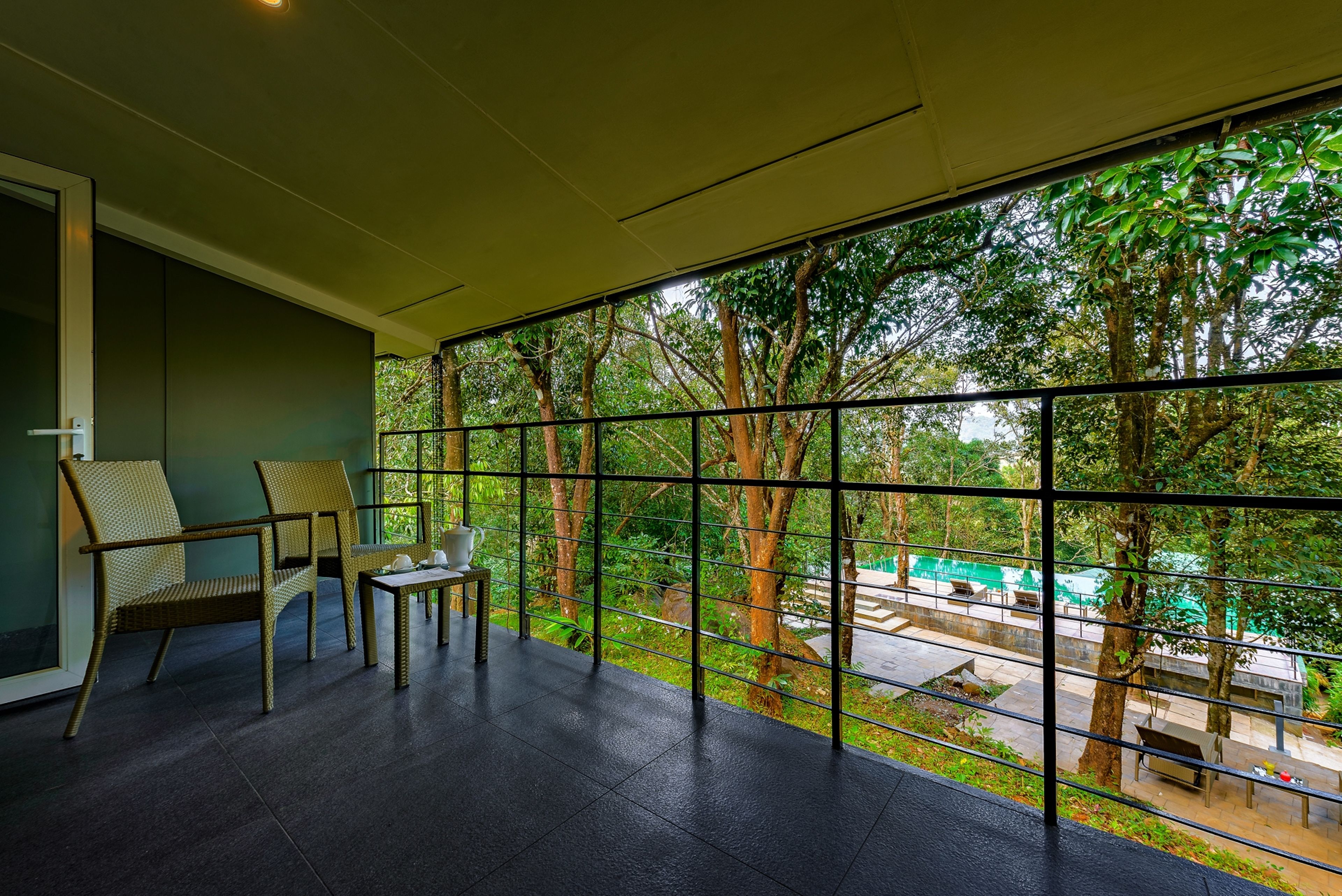 A room with a large window, a chair, a small table, and a view of trees and a pathway outside.