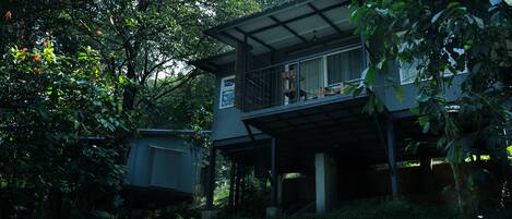A two-story house with a balcony, surrounded by dense foliage.