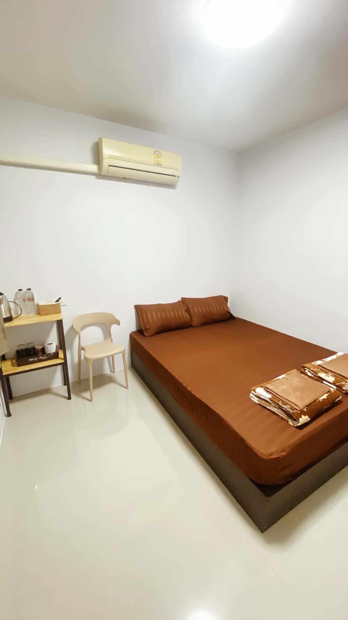 Un dormitorio con cama, una silla, una estantería con objetos y un equipo de aire acondicionado.