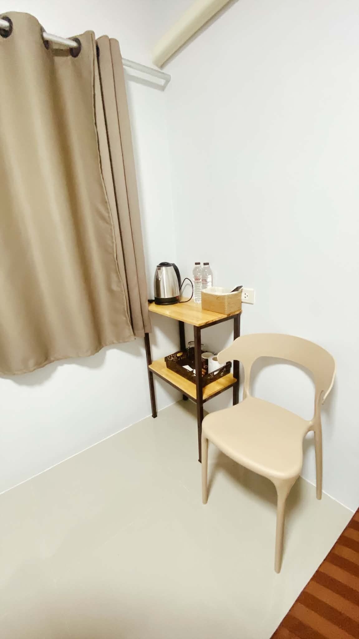A small room with a single chair, a table with a kettle, and a curtain.