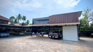 A parking area with several cars and a motorcycle, a covered structure, and a building with a modern design. - Ploynam Homestay (Amphawa)