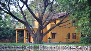 Un bâtiment jaune doté d’un balcon, entouré d’arbres et bordé d’un étang.