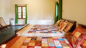 Une chambre à coucher avec un grand lit, une chaise en bois, une fenêtre avec des rideaux verts et un ventilateur de plafond.