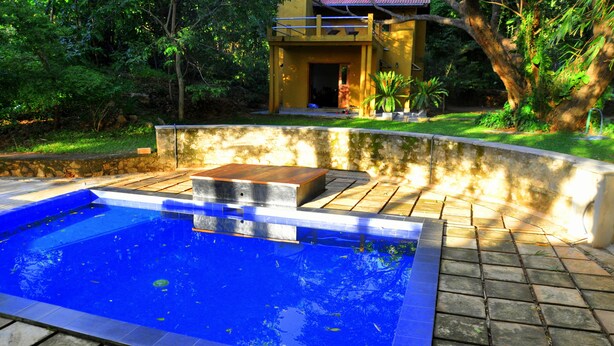 Une piscine bordée de pierres, une terrasse en bois et un bâtiment en arrière-plan.