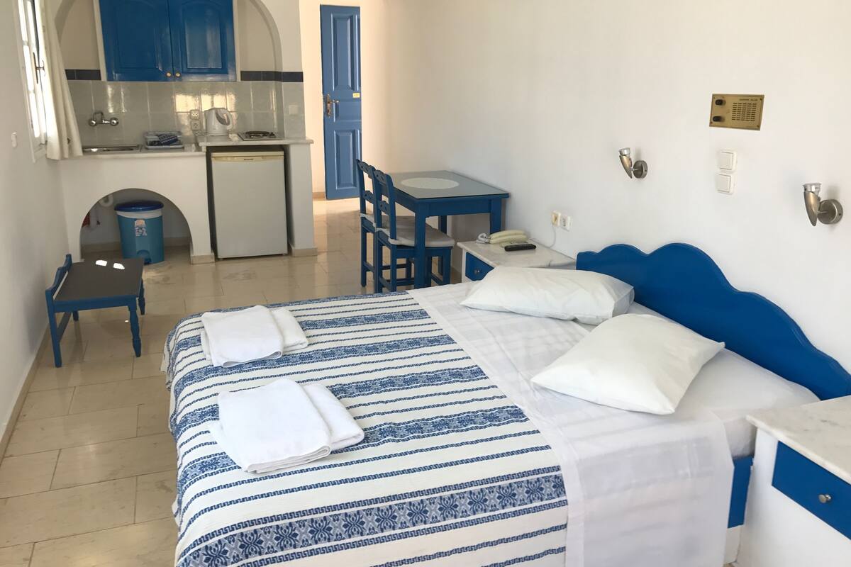 Ein Hotelzimmer mit Bett, Schreibtisch, Stuhl, einer kleinen Küchenzeile und einem Badezimmer.