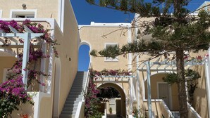 A narrow pathway flanked by white columns and arches, leading to a building entrance.