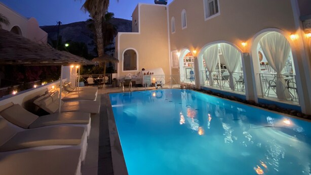 A poolside area with lounge chairs and a pool, surrounded by a building with arched windows and a palm tree.
