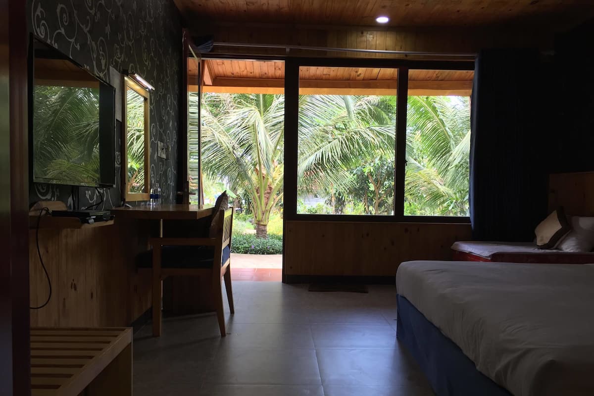A room with a bed, a desk, and a large window with a view of palm trees.