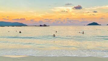 Uma praia com águas calmas, um cais ao fundo e montanhas ao longe.