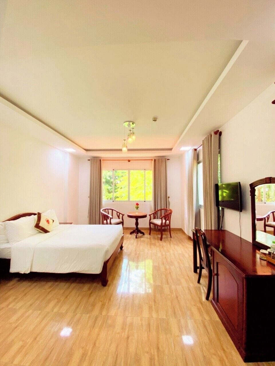 A hotel room with a bed, a dining table with chairs, a television, and a large window with curtains.