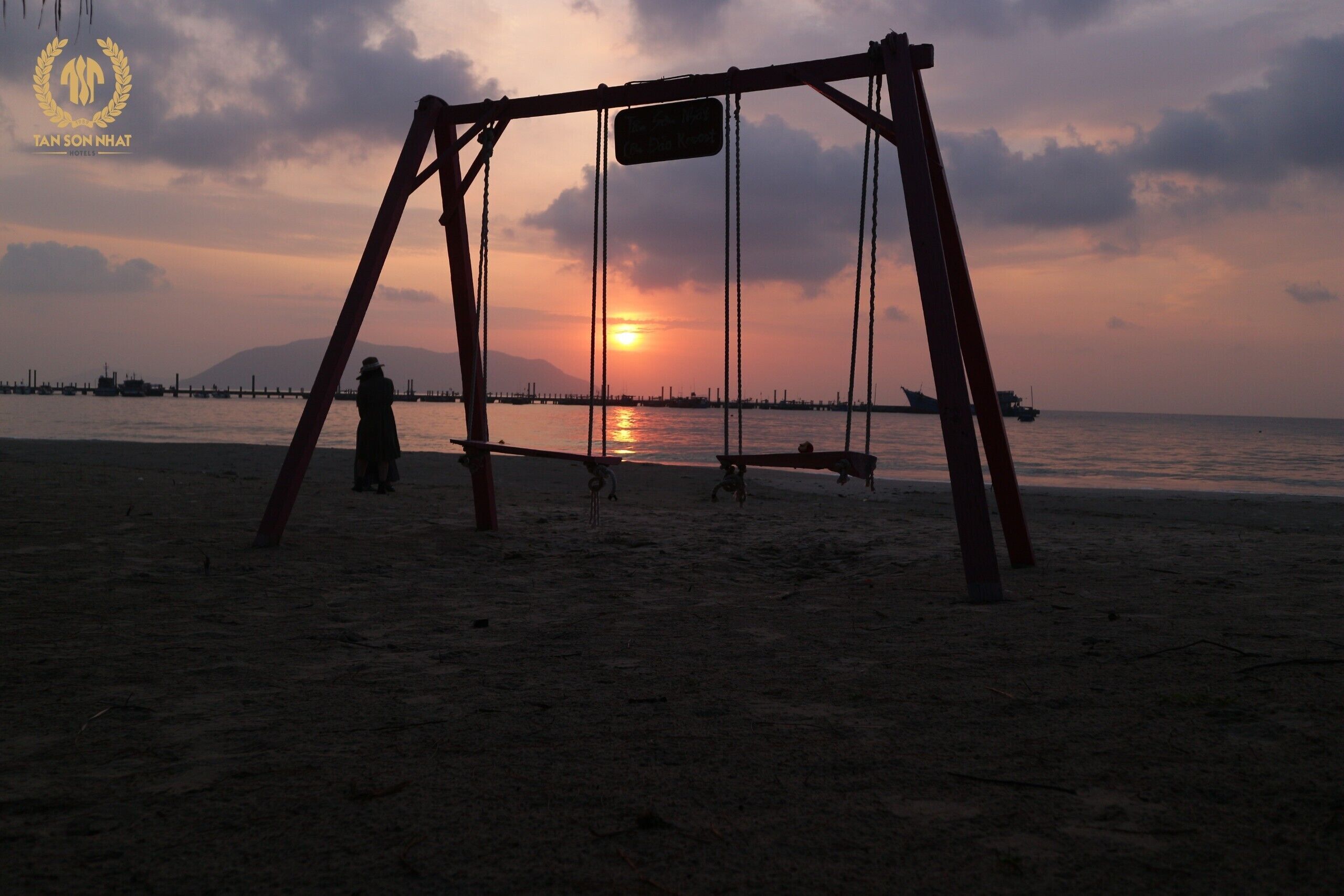 A swing set on a beach with a sunset in the background.