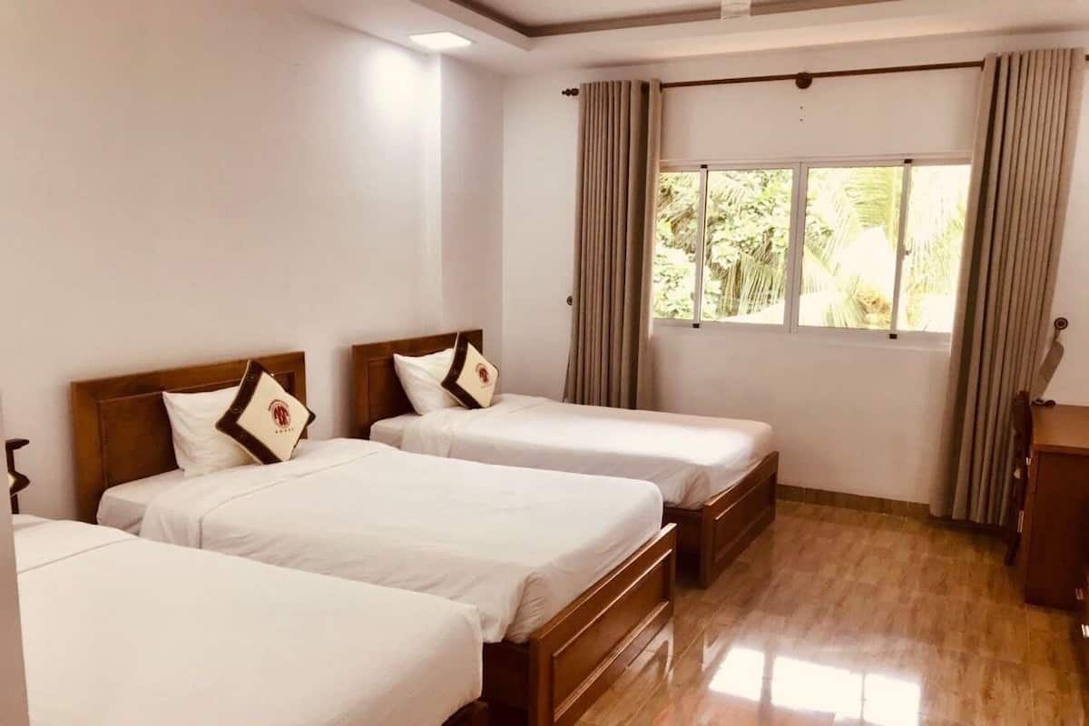 A hotel room with three single beds, wooden headboards, white bedding, and a large window with curtains.