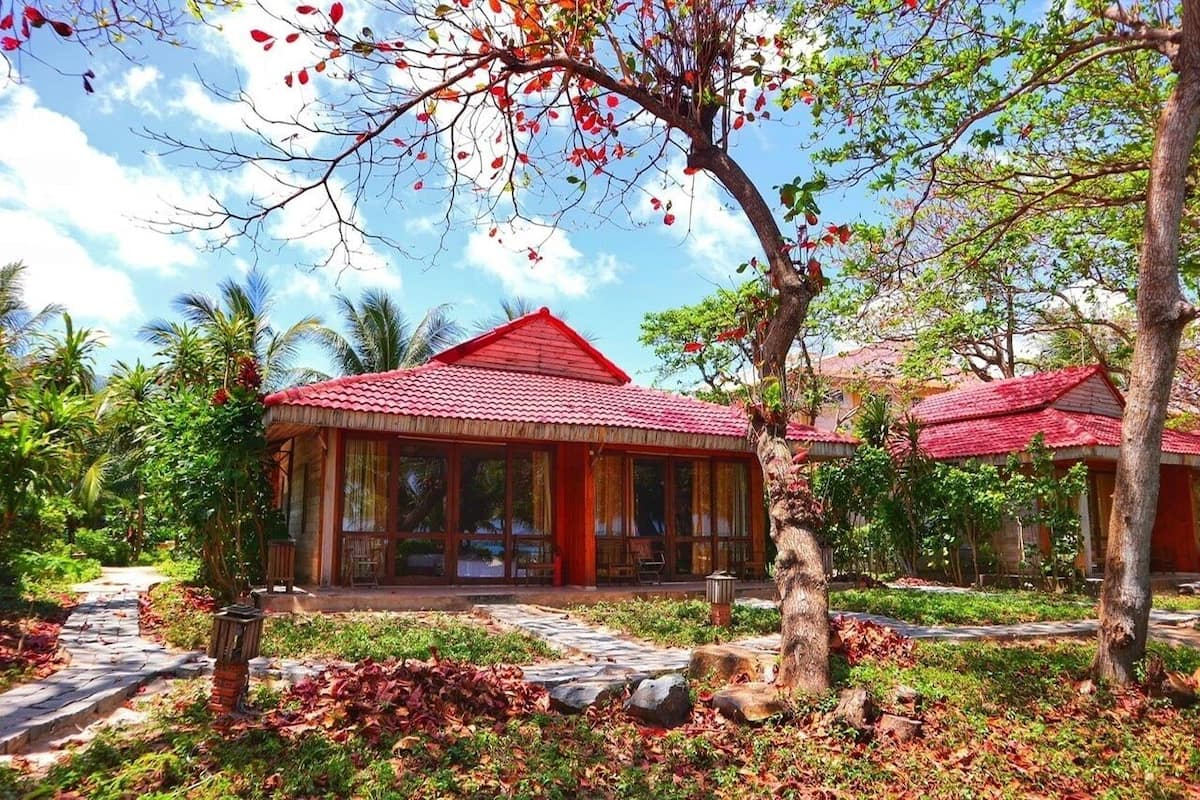 A traditional-style building with a red roof, surrounded by lush greenery and palm trees.