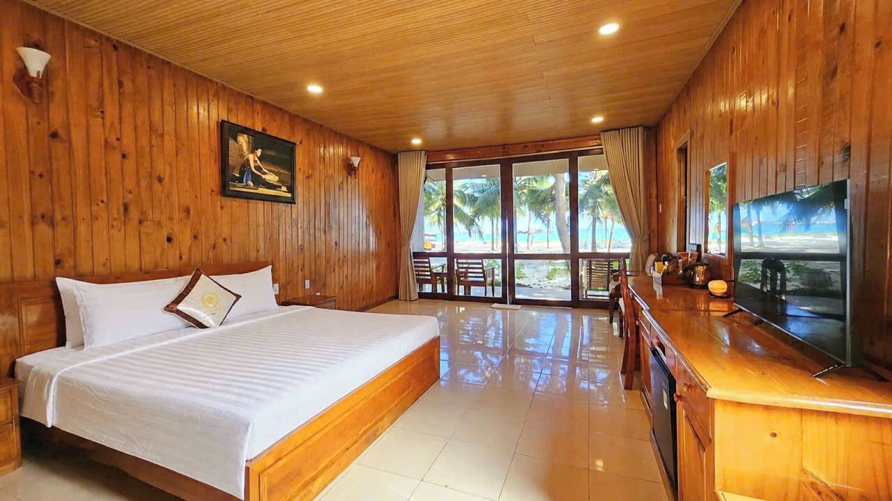 A wooden-paneled room with a bed, a television, and a view of the beach.