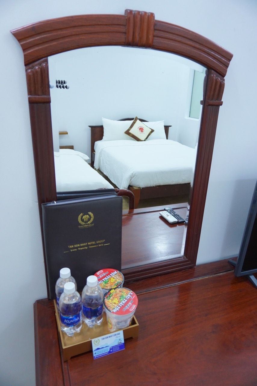 A hotel room with a bed, a desk, a mirror, and a tray with bottled water and snacks.